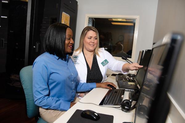 A nursing administrator working with a Health Informaticist at a computer. 